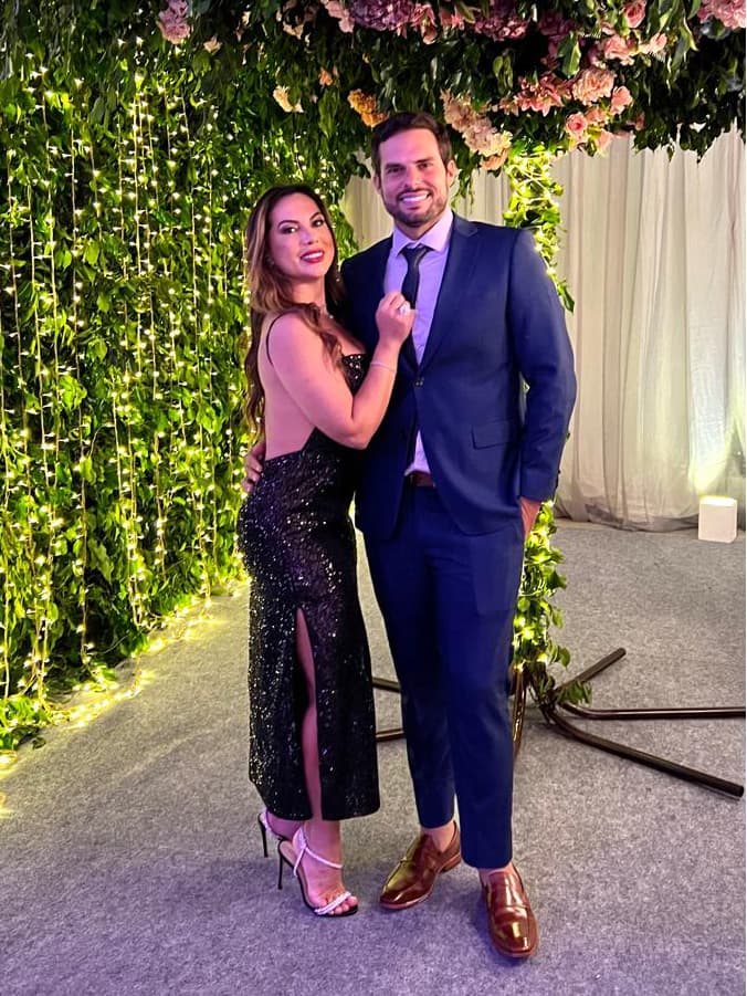 Gina e José Carlos posam juntos sob uma estrutura floral iluminada.